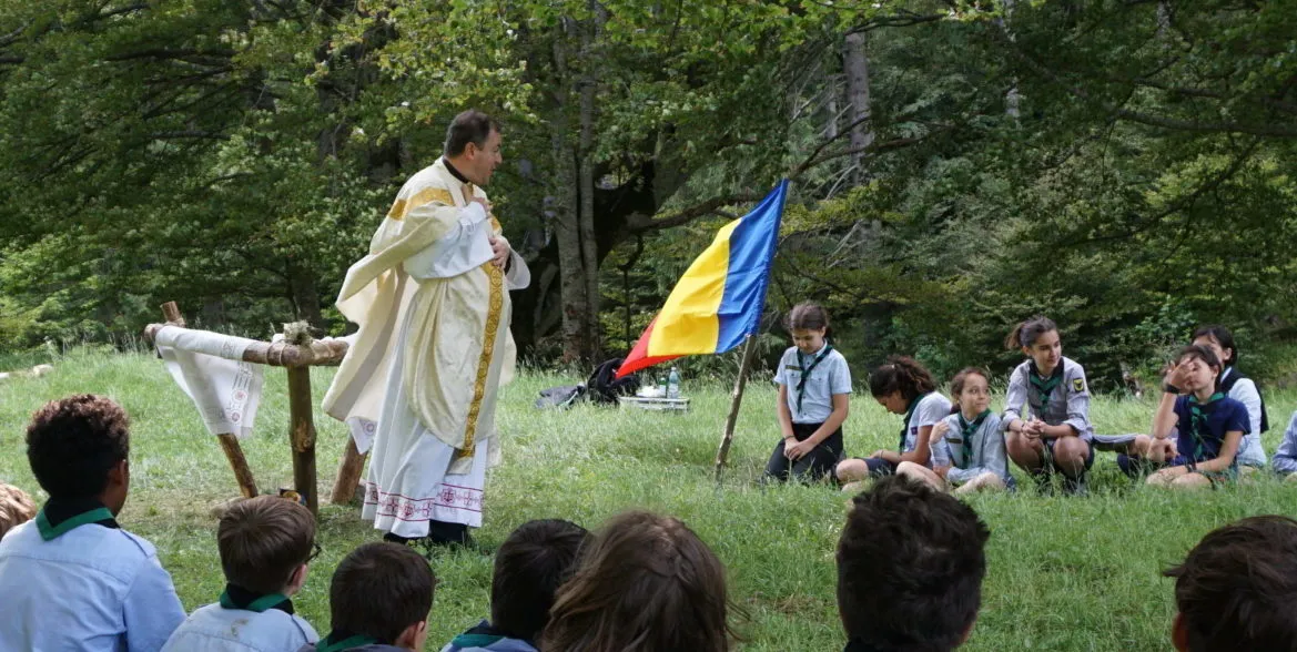 Preotul celebrează Liturghia în tabără, în fața cercetașilor așezați pe iarbă.